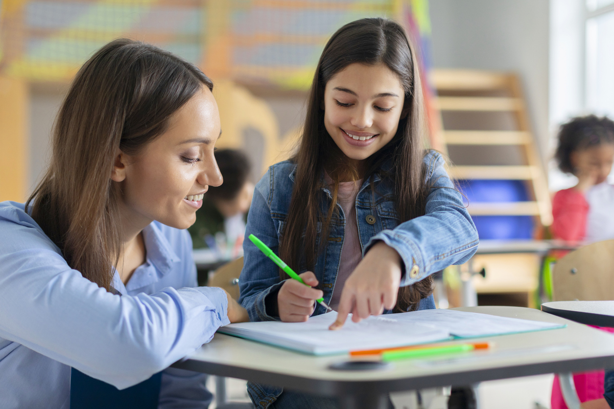 A smiling teacher helps a student working on an assignment.