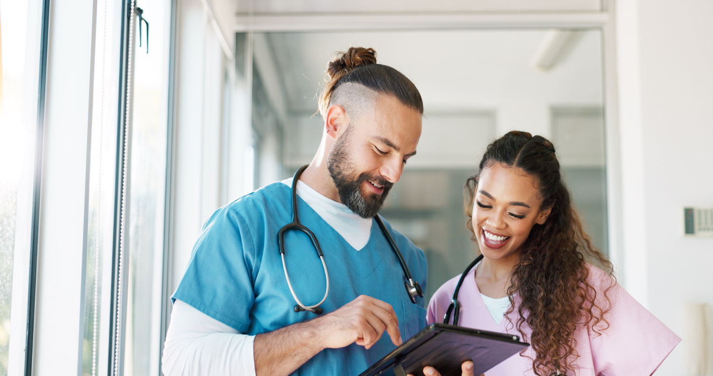 Two Nurses Smiling and Working on a Tablet in a Medical Facility.