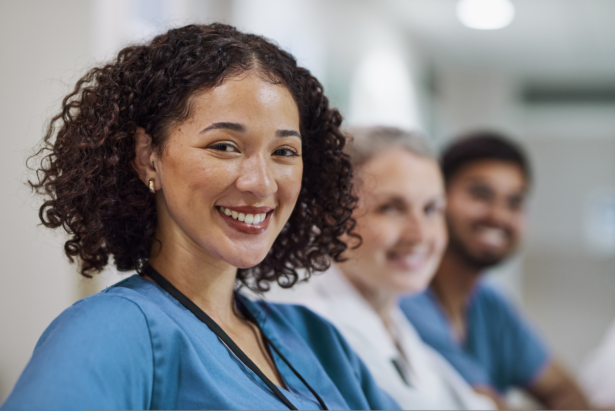 A smiling nurse with two other caregivers in the background.