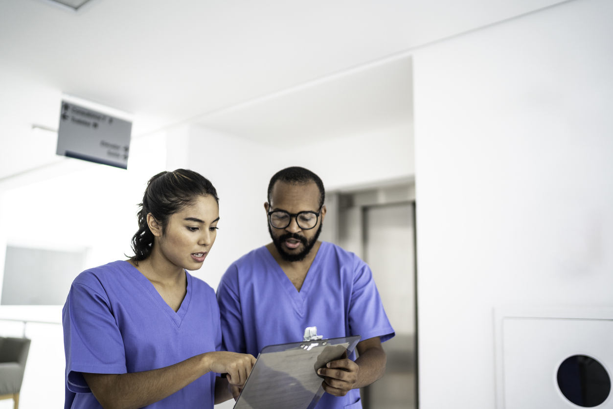 A travel nurse looking at a clipboard with another nurse in a medical facility.