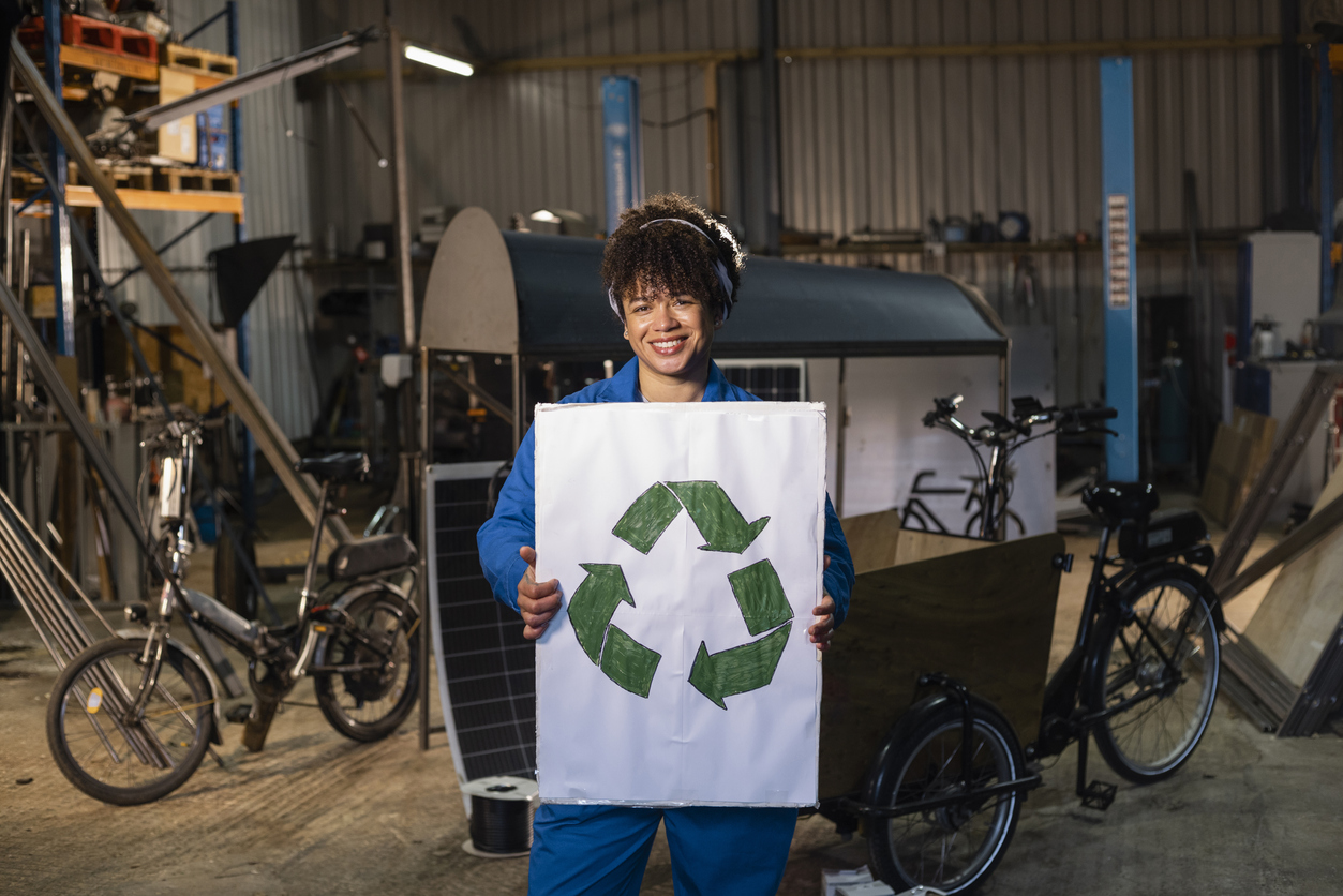A small business owner holds a recycling sign in a workshop where electric bikes are built.