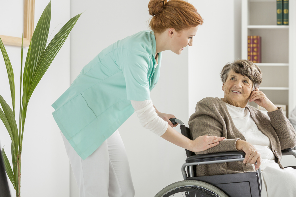 A Nurse Practitioner Leaning Over and Talking With an Older Patient in a Wheelchair.