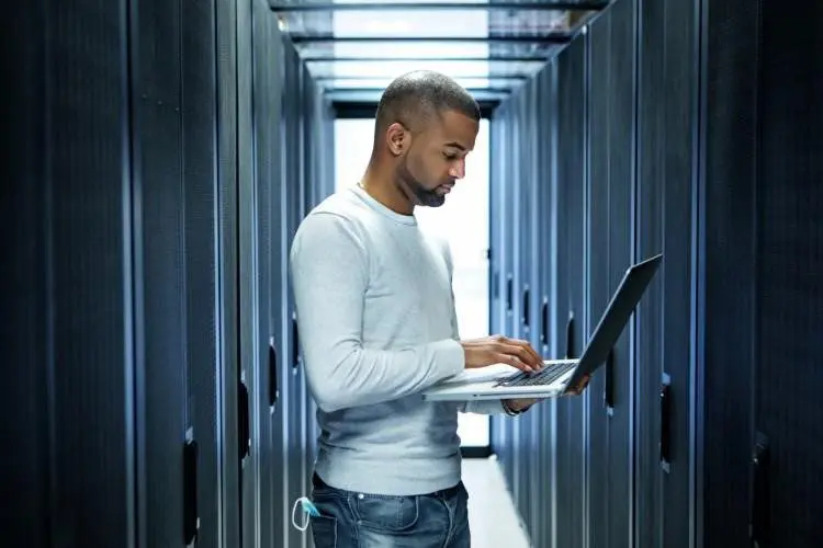 A Technology Management Worker Holding a Laptop in a Server Room.