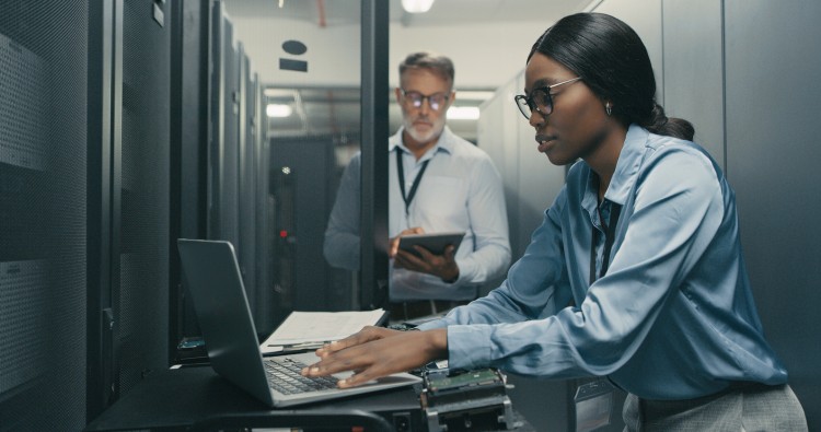 Two cybersecurity professionals working on laptops in a data center.