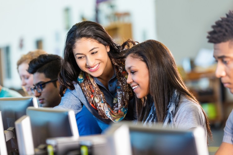 A teacher helps students working on individual computers.