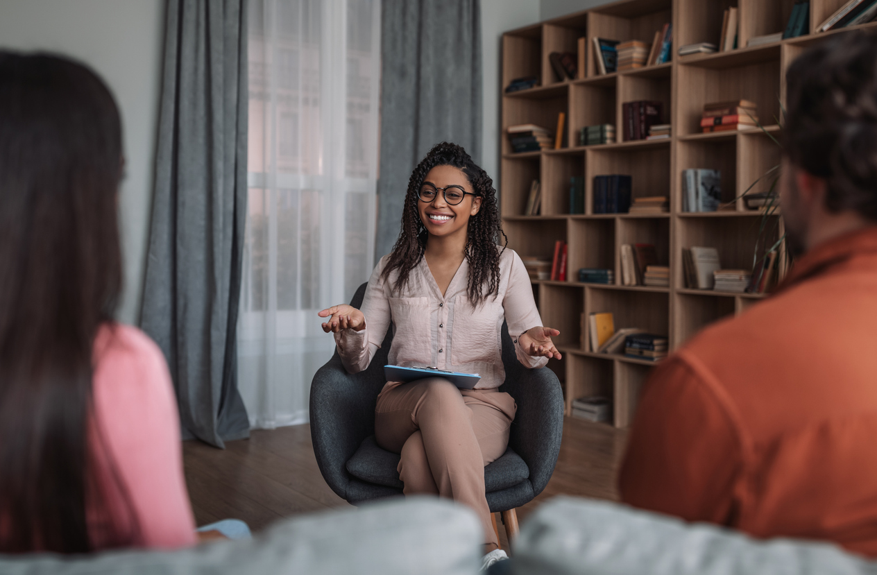 A smiling psychologist talks with two clients in a counseling office.