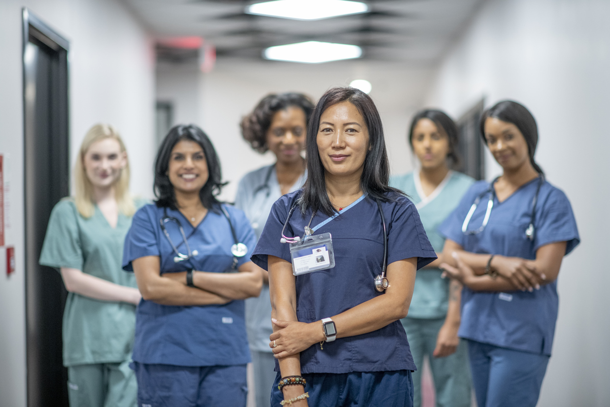 A smiling nurse leader stands in front of other care providers in a hospital corridor.