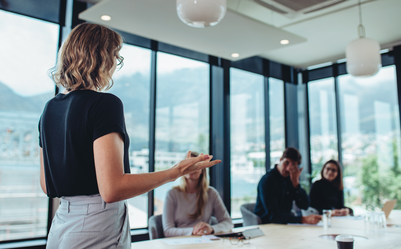 A team leader speaks to a group of employees seated at a conference table.