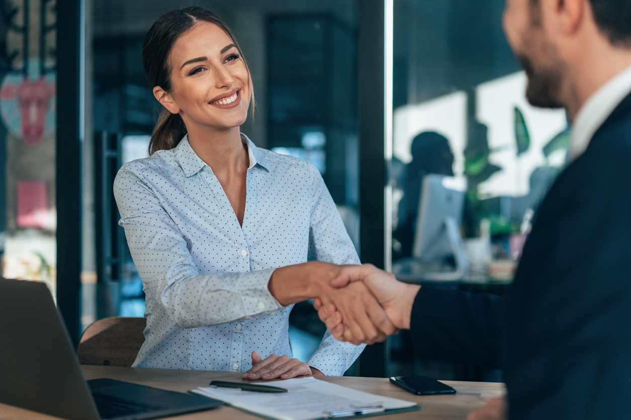 A smiling human resources specialist shakes hands with a new hire.