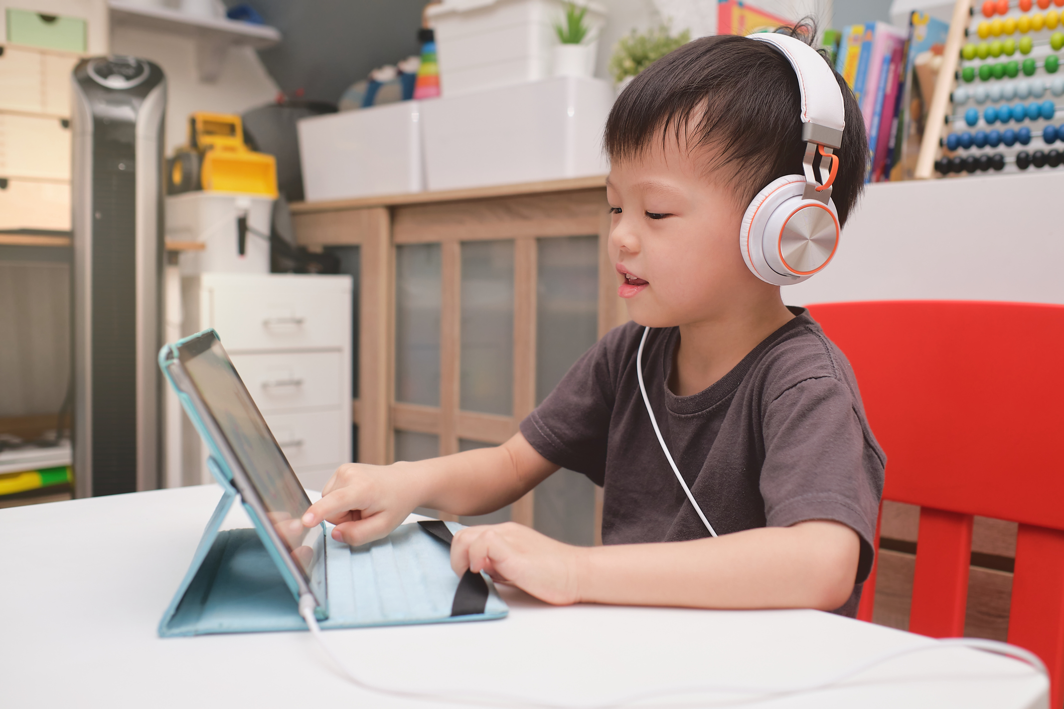 A toddler wearing headphones using an education app on a tablet