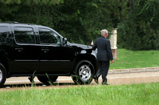 A Secret Service agent walks next to a black SUV in a motorcade.