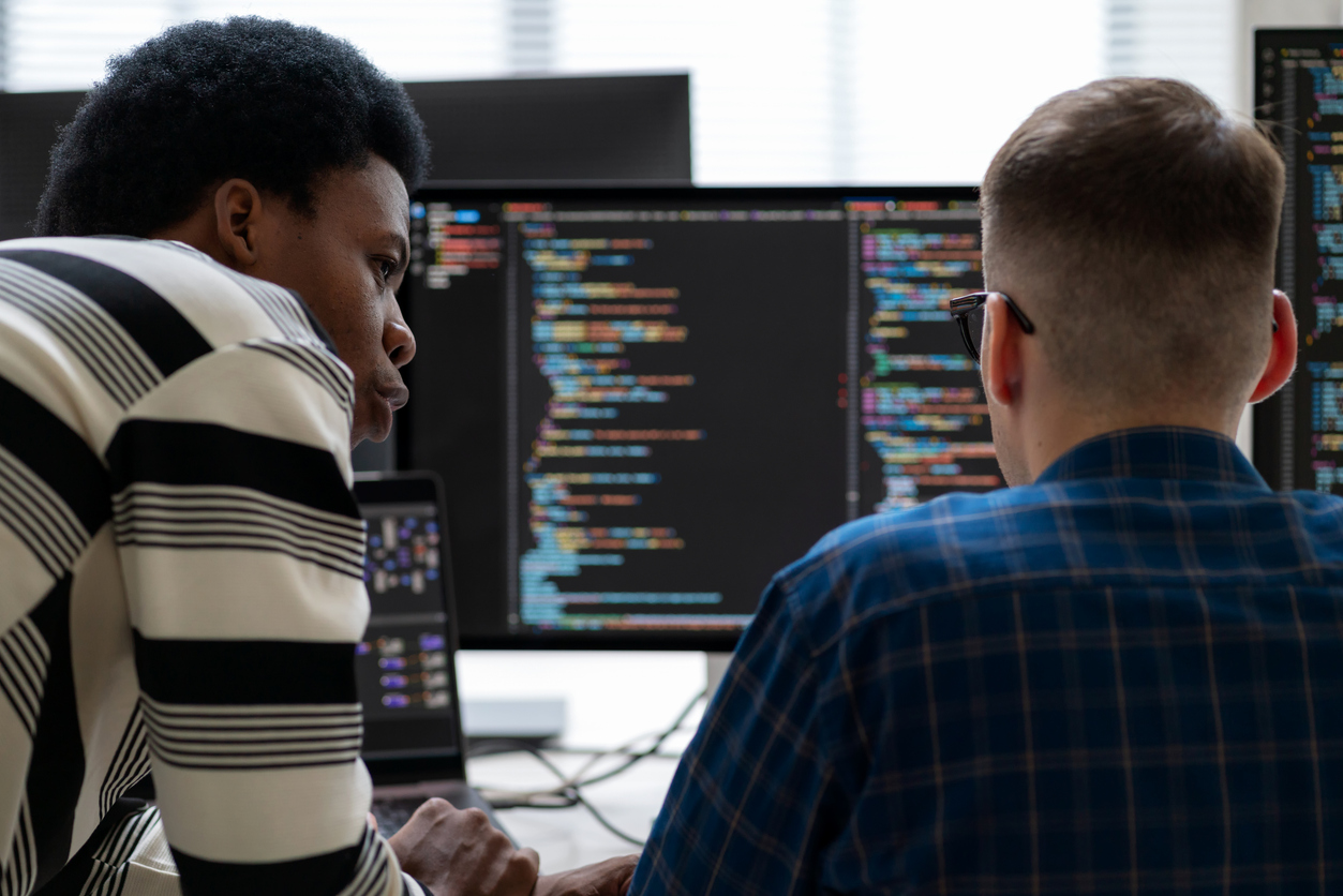 Two cybersecurity professionals review code on an array of monitors.