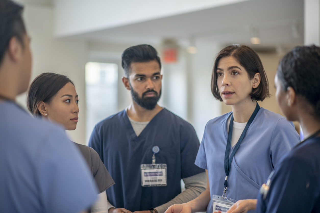 An Aprn Speaks With a Team of Nurses in a Hospital Hallway.