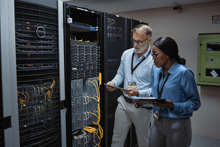 Network administrators in a server room use a tablet to analyze network performance.