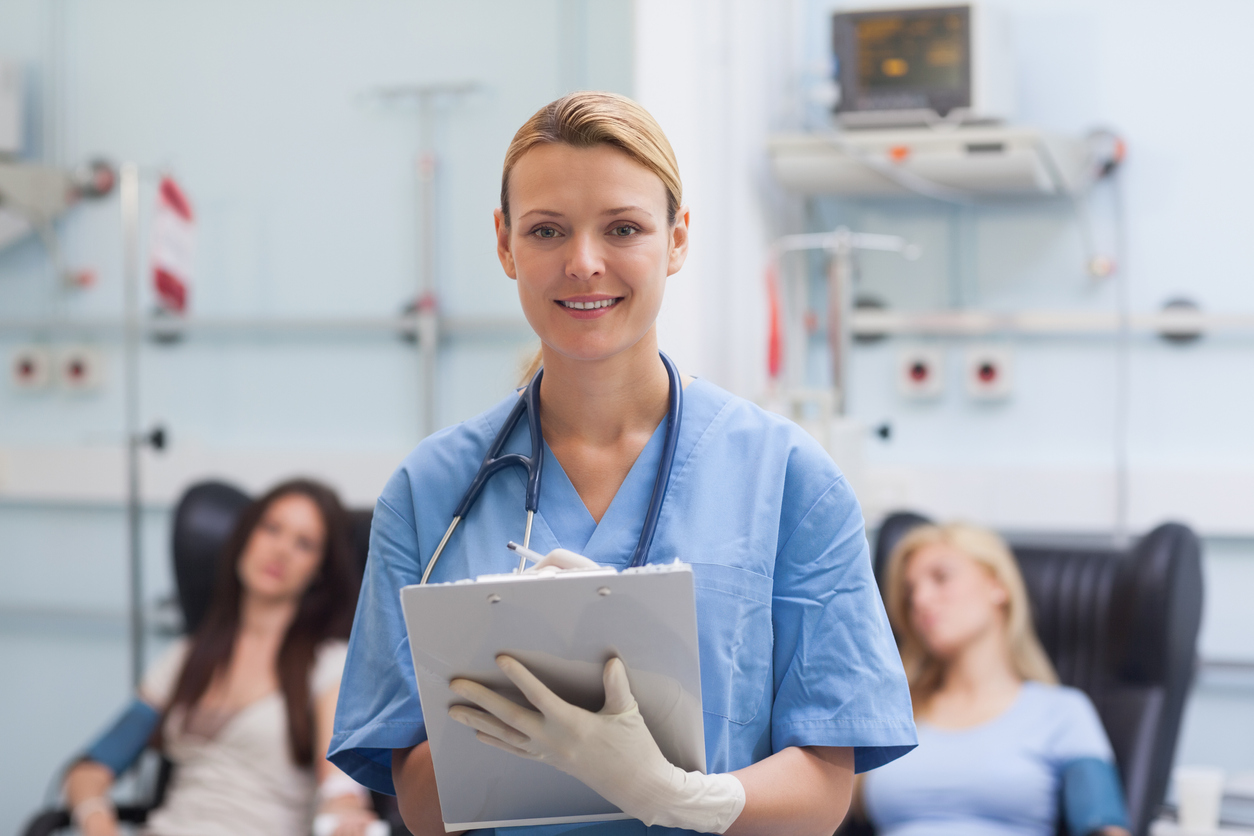 A nurse writing on a clipboard in a hospital room with two patients.