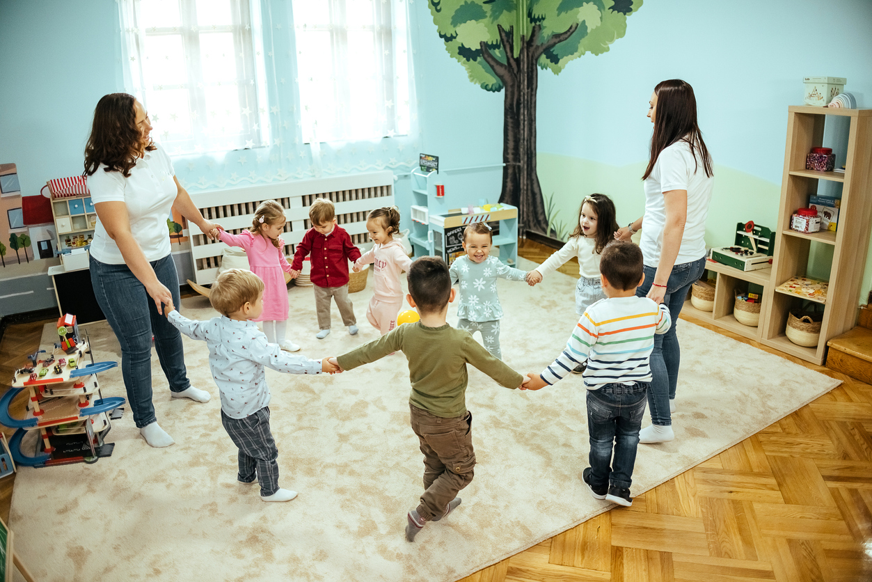 Preschool Students and Two Teachers Hold Hands and Dance in a Circle in Class.