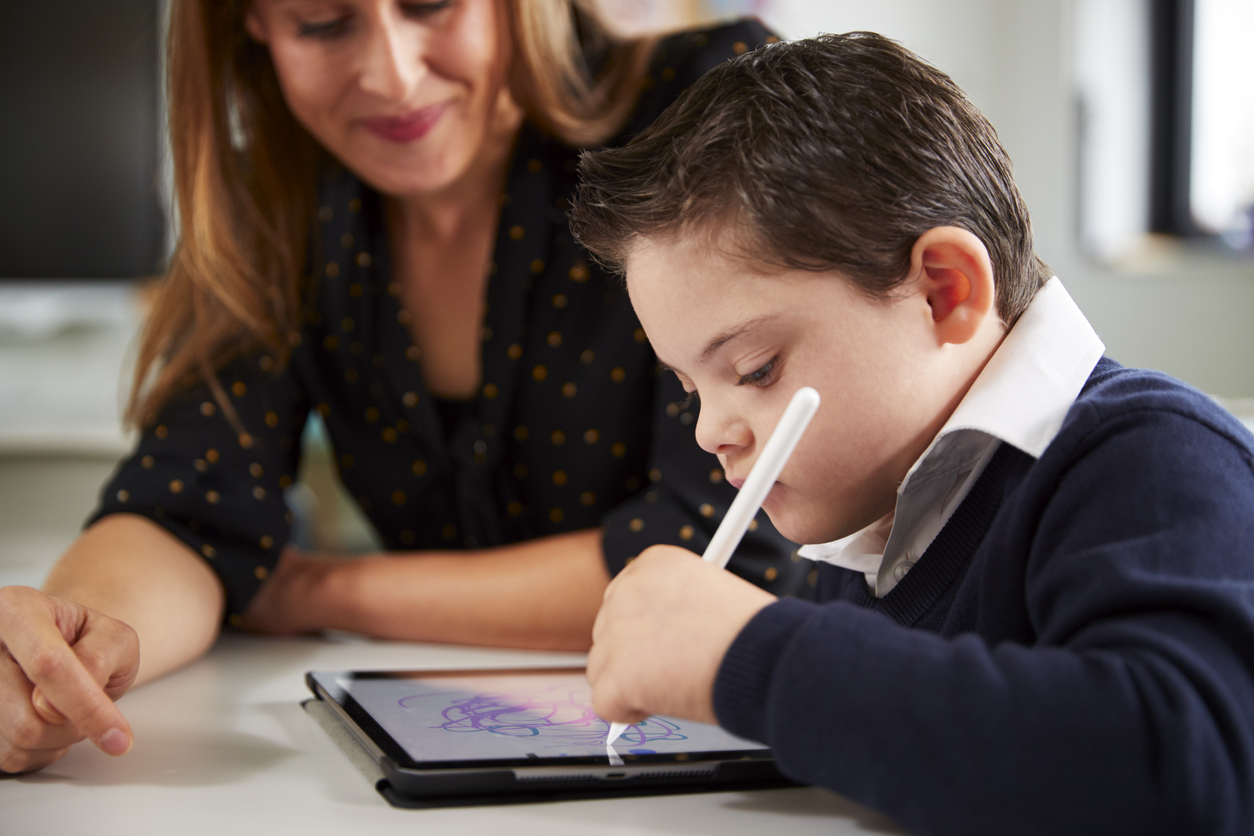 A Special Education Teacher Works With a Student With Down Syndrome Drawing on a Tablet.