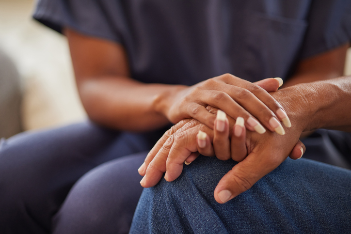 A nurse’s hands clasping a patient’s hand, shown in close-up.