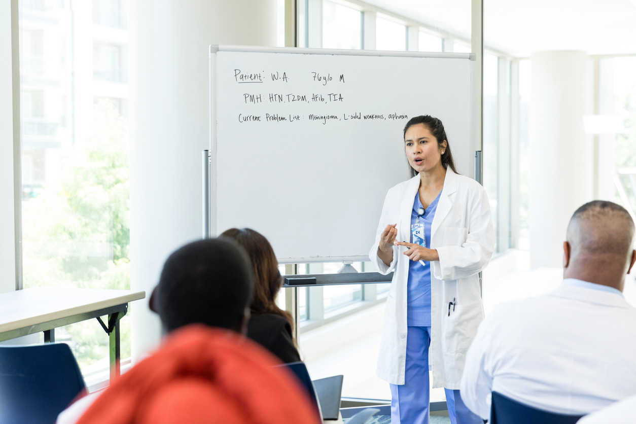 A Nurse Leader in Front of a Whiteboard Gives a Presentation to Seated Students.