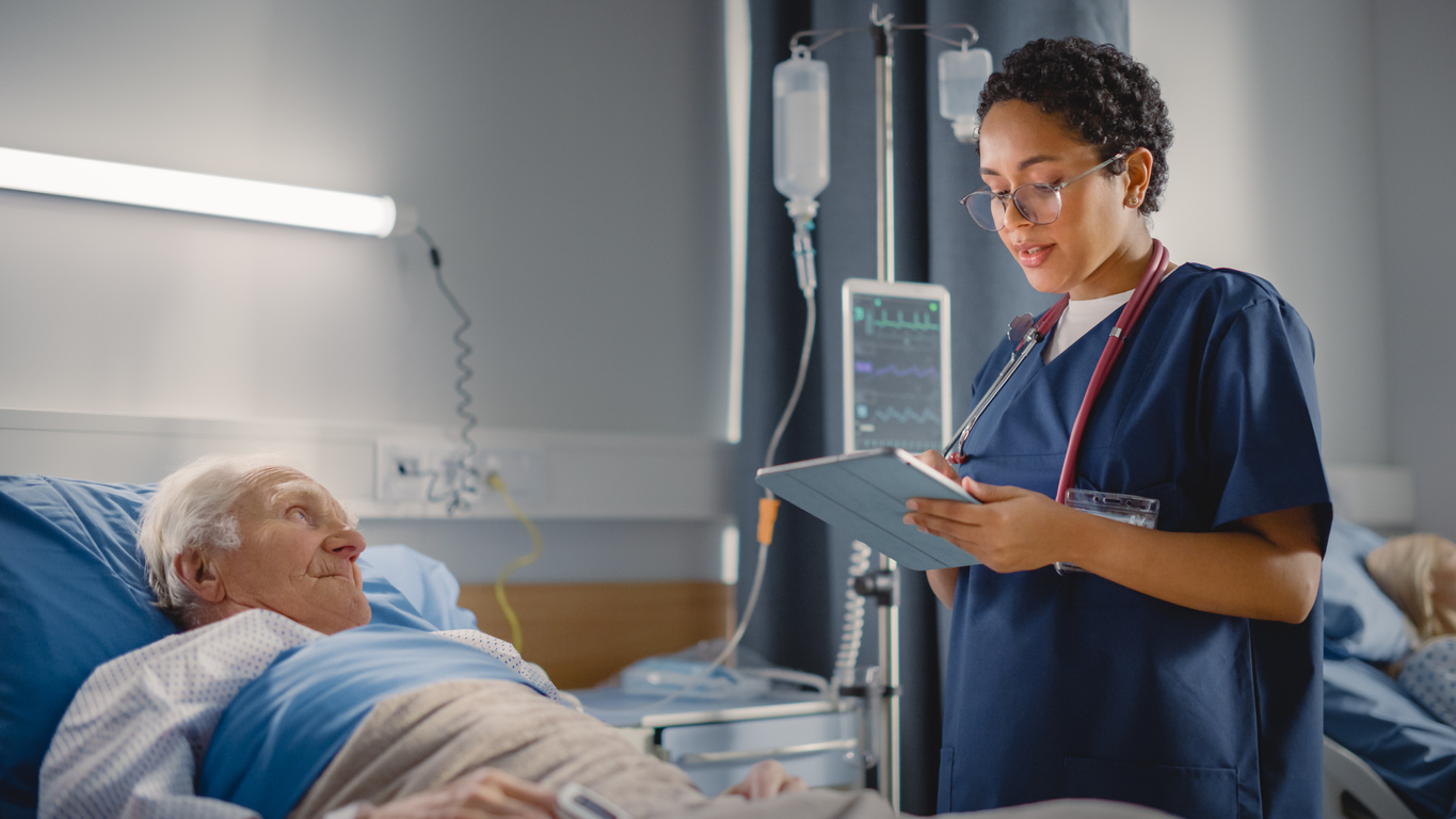 A clinical nurse specialist consults with a patient in a hospital bed.