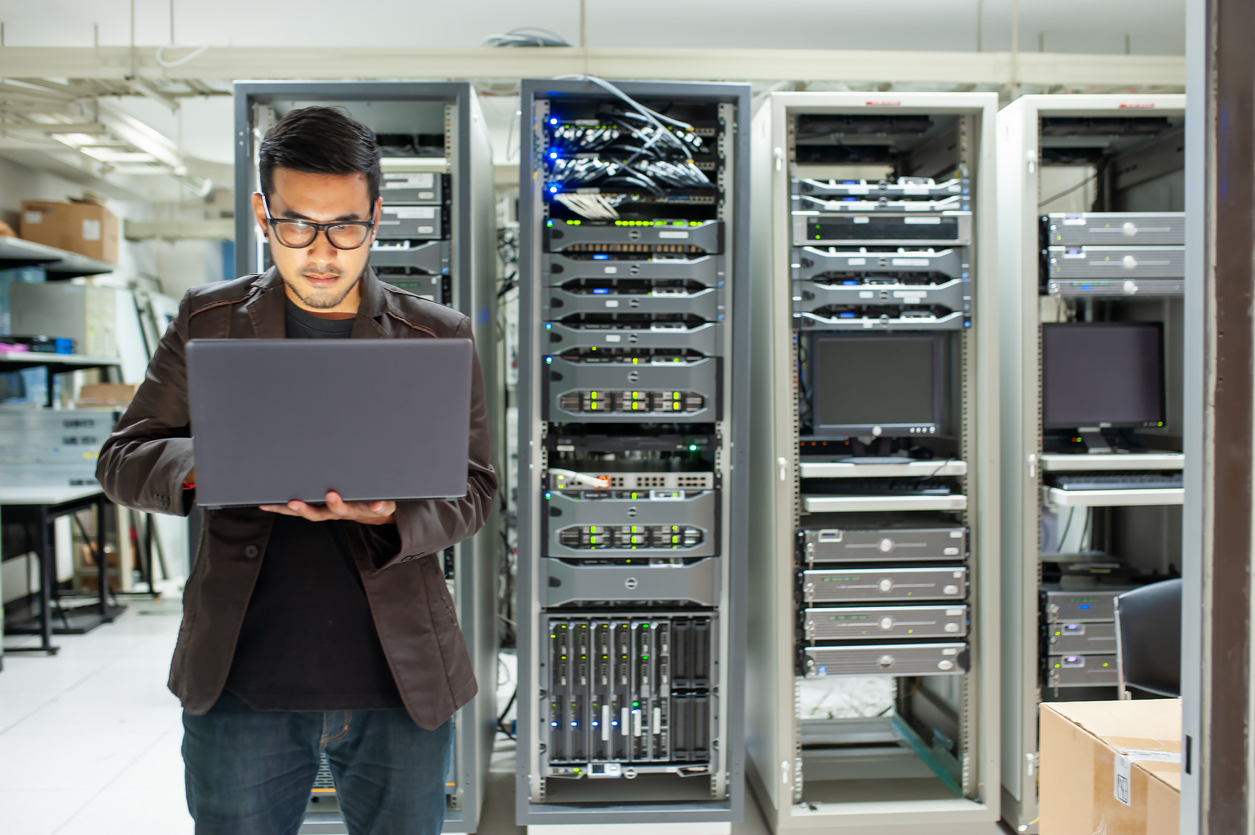 An Information Technology Professional Standing in a Server Room Holding a Laptop.