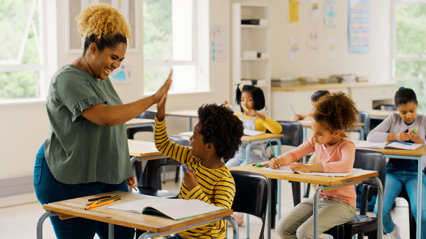 A teacher high-fives a student in a classroom.