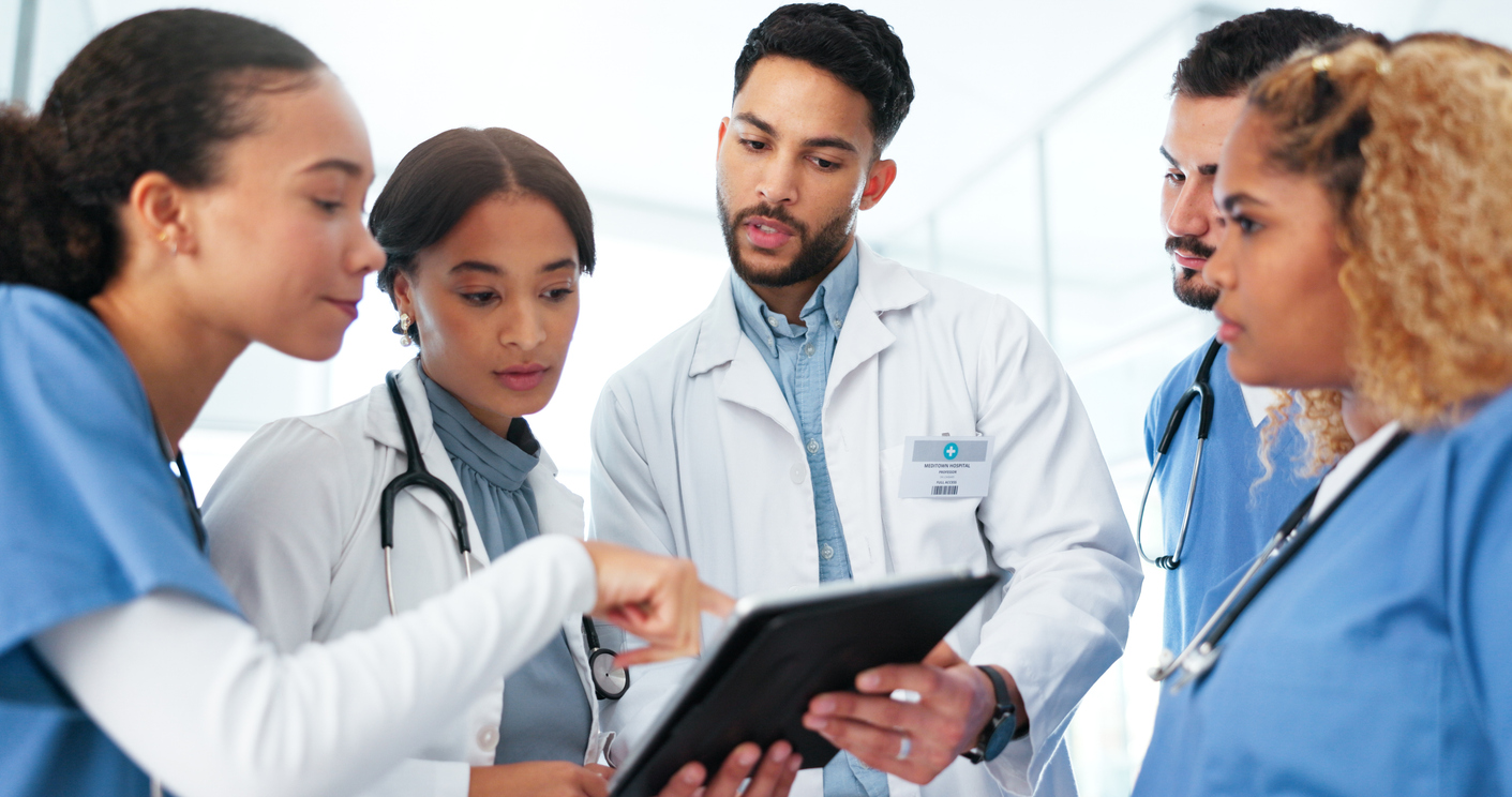 A group of medical professionals standing and looking at a tablet.