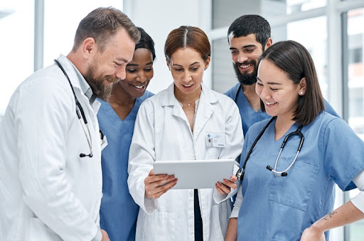A group of health care workers talking around a doctor holding a tablet.