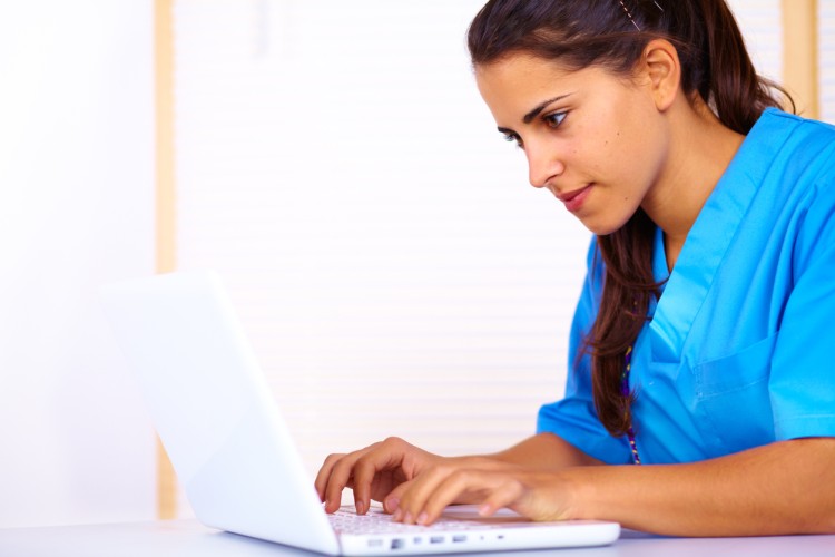 A registered nurse types on a laptop.