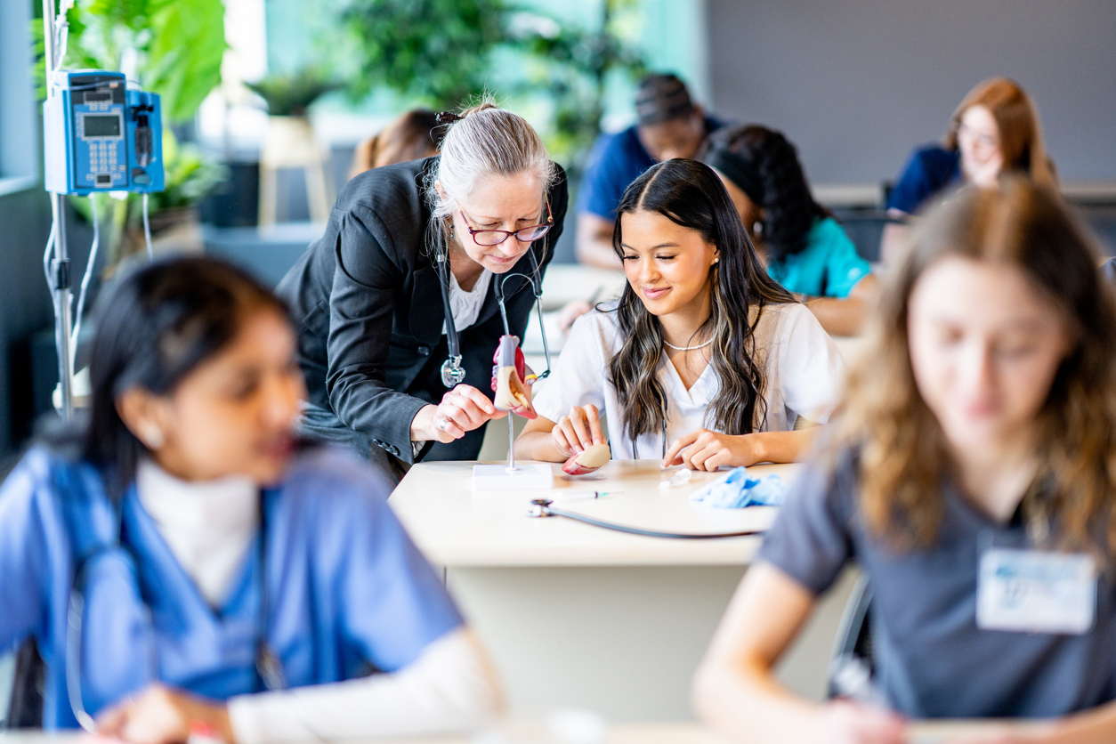 A professor works with a nursing student in a classroom.