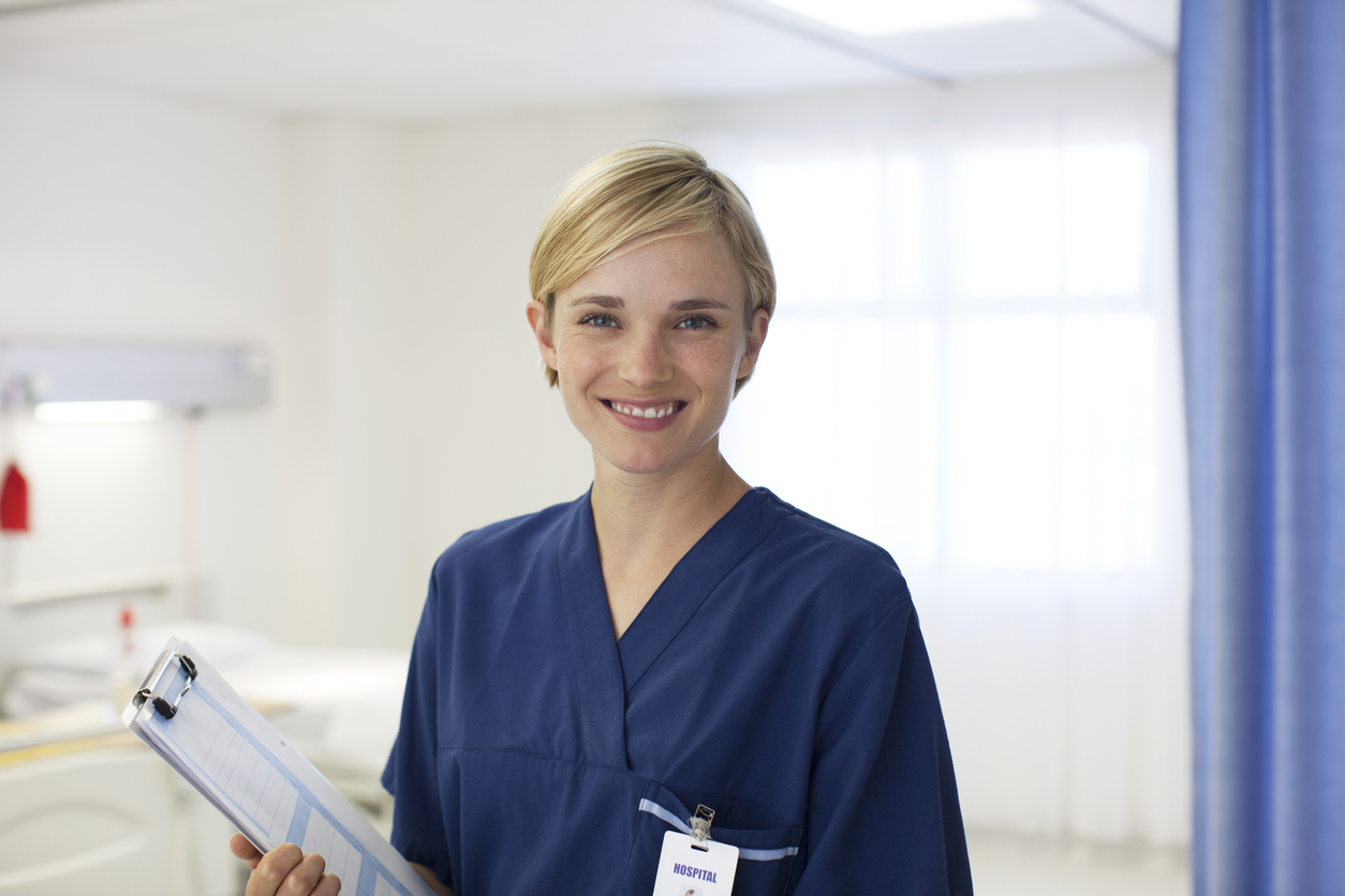 Nurse Standing in a Hospital Room Wearing Scrubs and Holding a Clipboard.