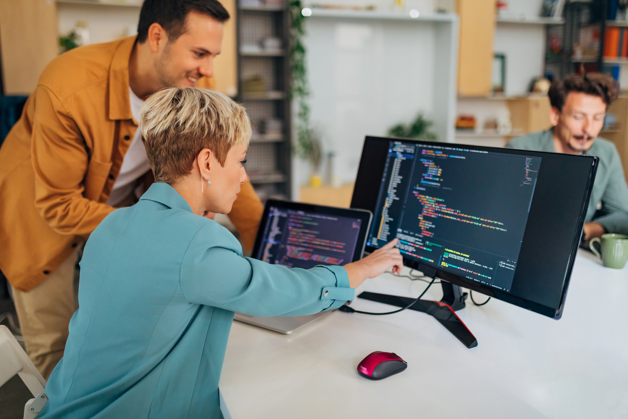 Two programmers discuss a line of code while looking at a computer monitor.