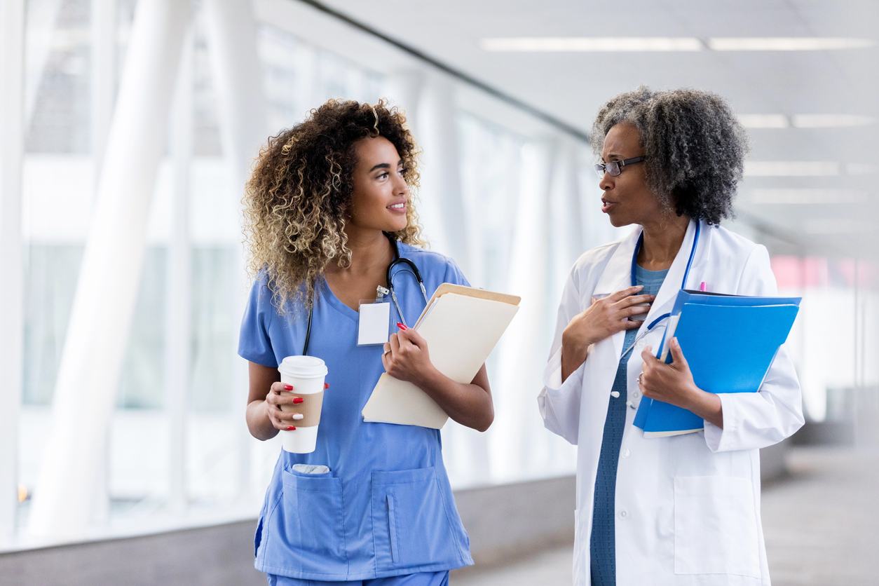 A Nurse Mentor Talks With Their Mentee While Walking Down a Hospital Corridor.