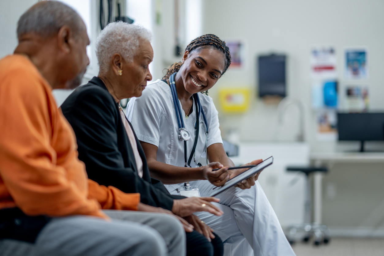 A Smiling Nurse Shows a Patient a Tablet While a Family Member Looks On.