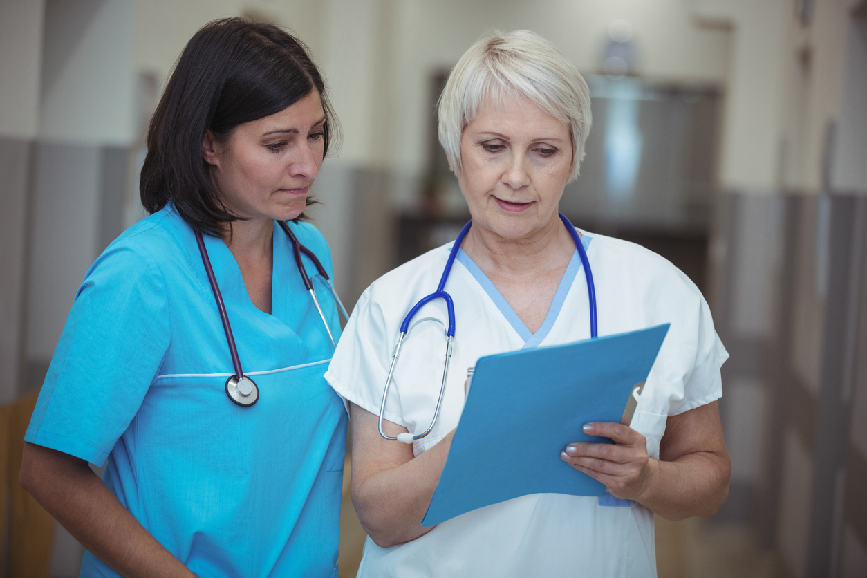 Nurses talking and looking at a chart in a hallway of a medical facility.