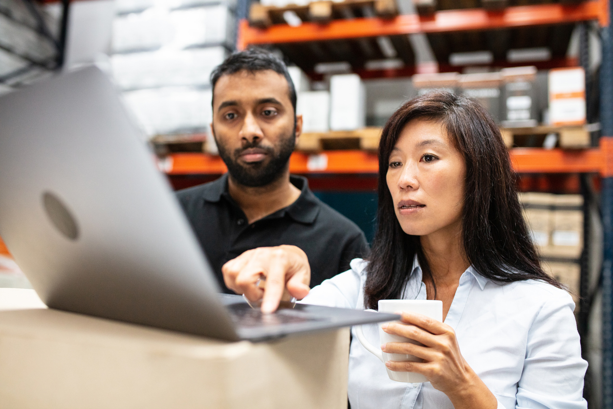 An inventory manager reviews information on a laptop with a member of the warehouse staff.