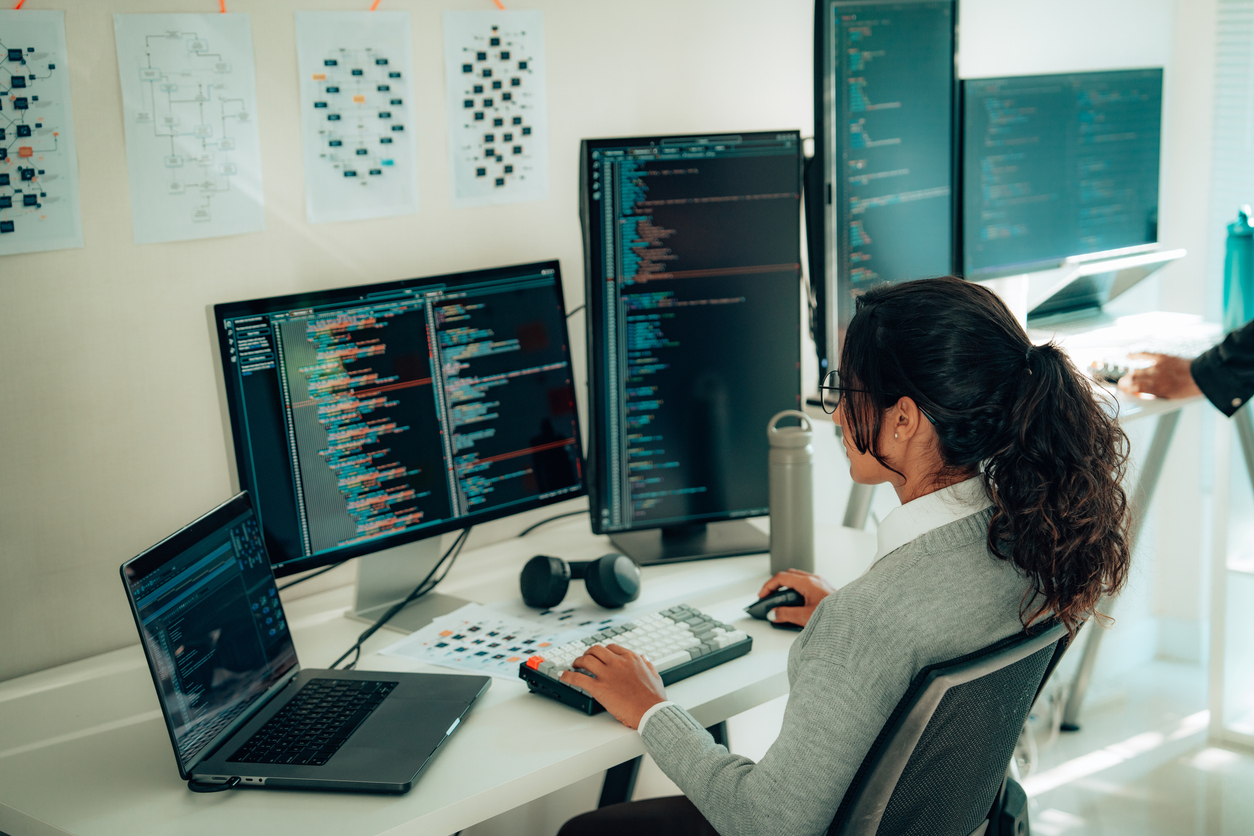 A cybersecurity professional reviews code on a bank of monitors.