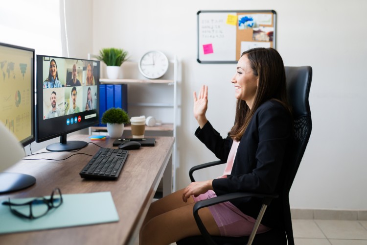 A Remote Worker Waves at Colleagues on a Computer Screen During a Videoconference.