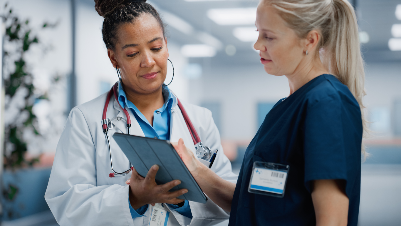 A nurse manager shares information on a tablet with a nurse.