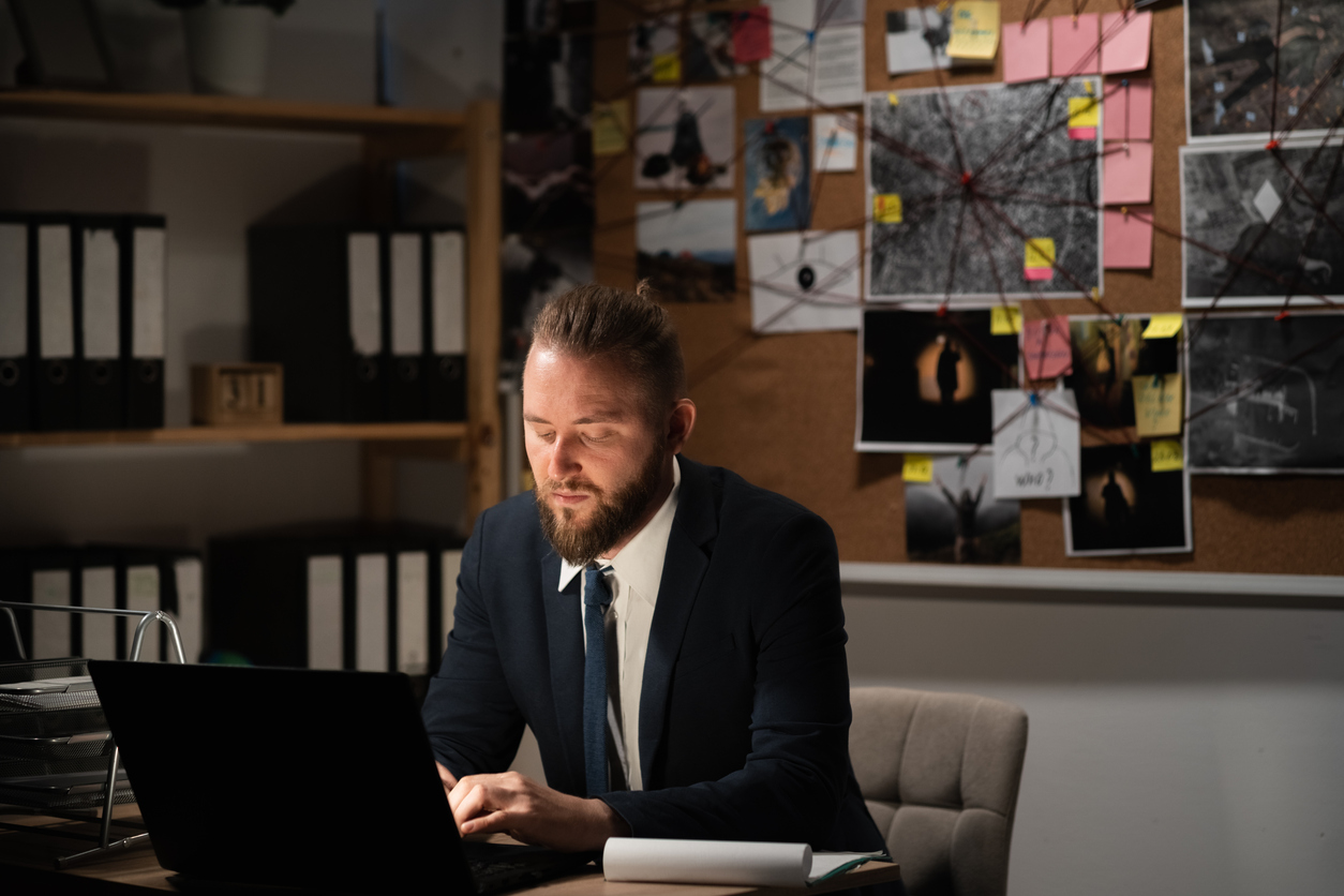 A Criminologist Works on a Laptop in Front of an Evidence Board.