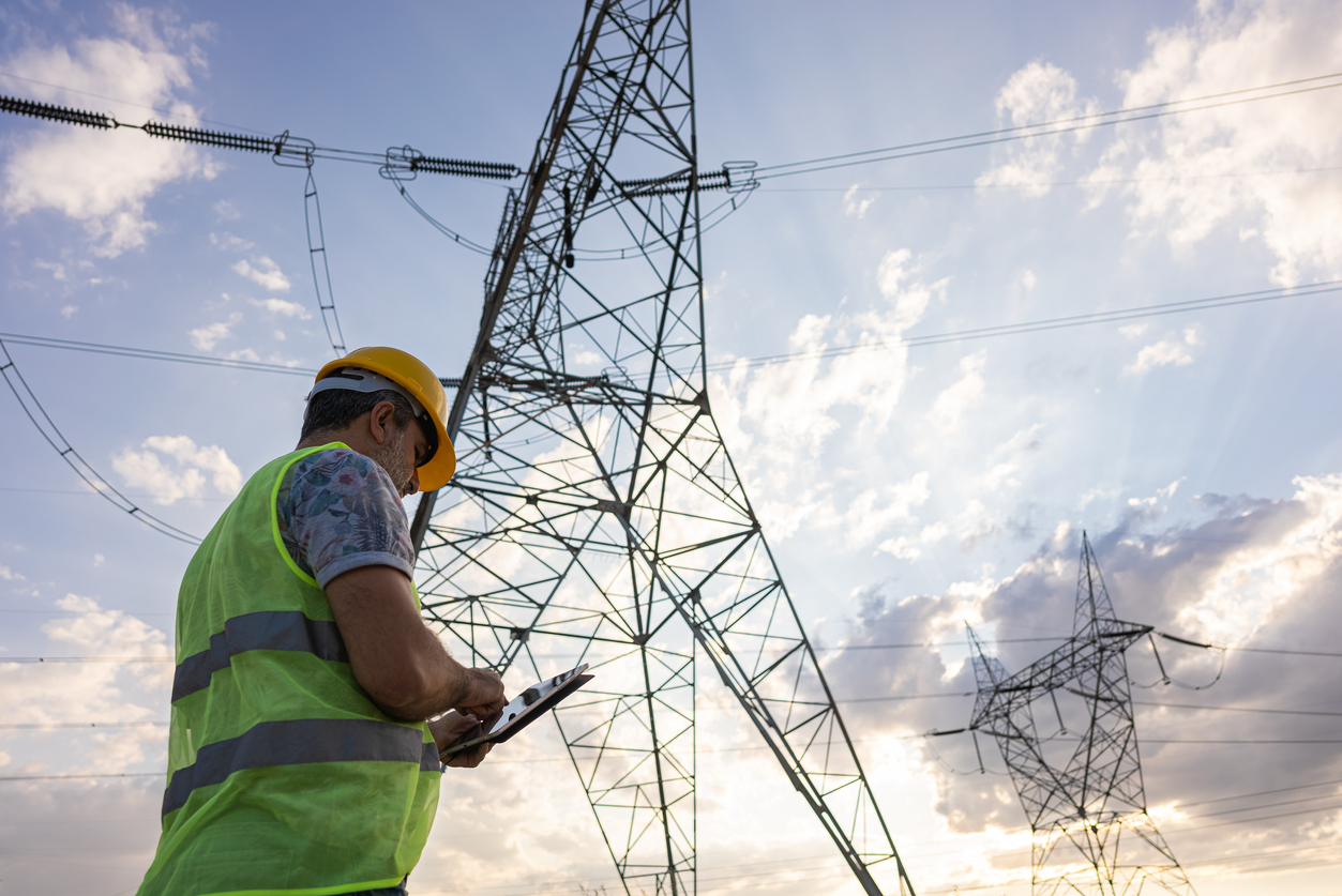 Engineer Looking at High Voltage Power Lines Uses a Tablet to Record Information.