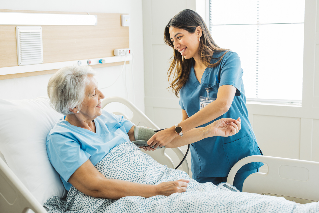 A Nurse Straps a Blood Pressure Cuff to a Patient’s Arm as They Lie in a Hospital Bed.