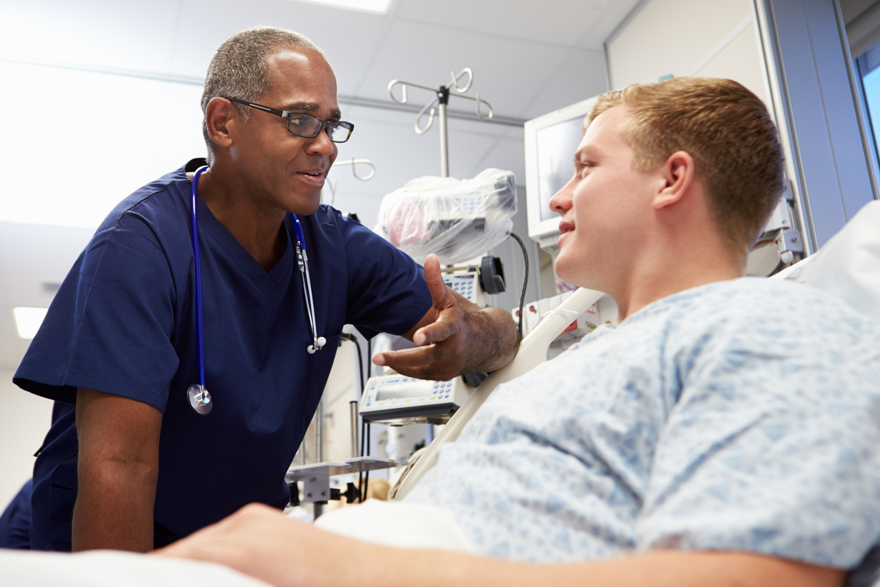 An acute care nurse practitioner speaks with a patient in a hospital bed. 