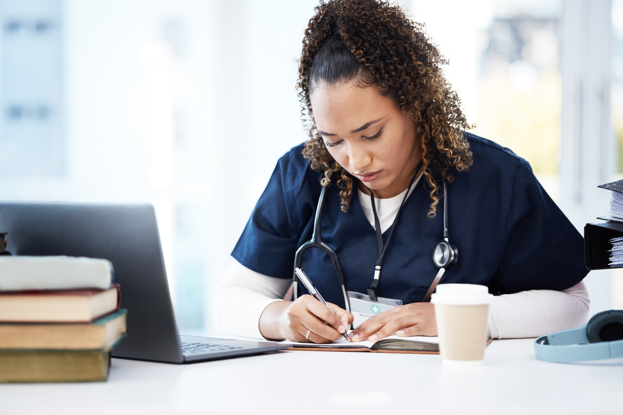 A nursing student in scrubs studying with a laptop.