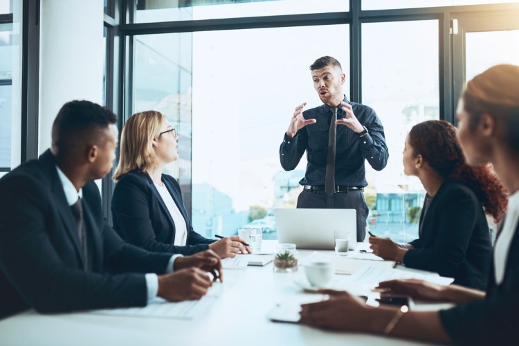 A businessperson gives a presentation to executives around a conference table.