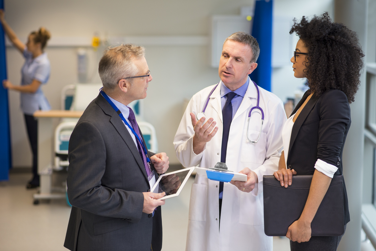 Two hospital administrators talk with a care provider in a hospital hallway.