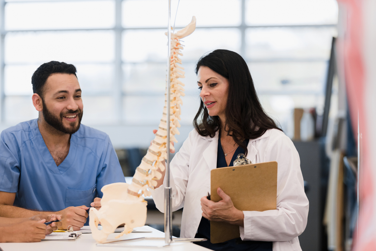 A nursing instructor points to a model of a human spine for a student.