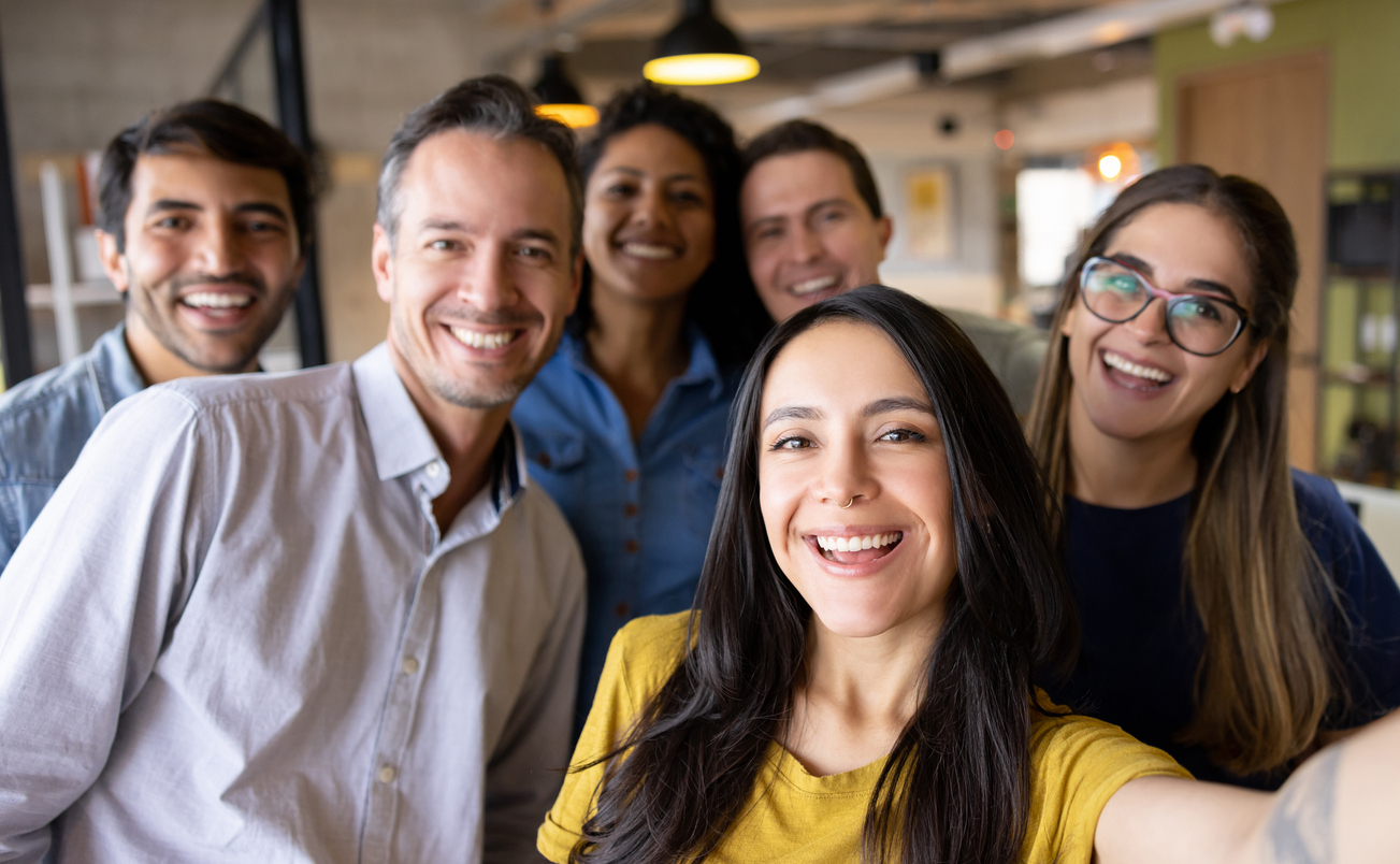 A group of happy co-workers take a selfie in an office.