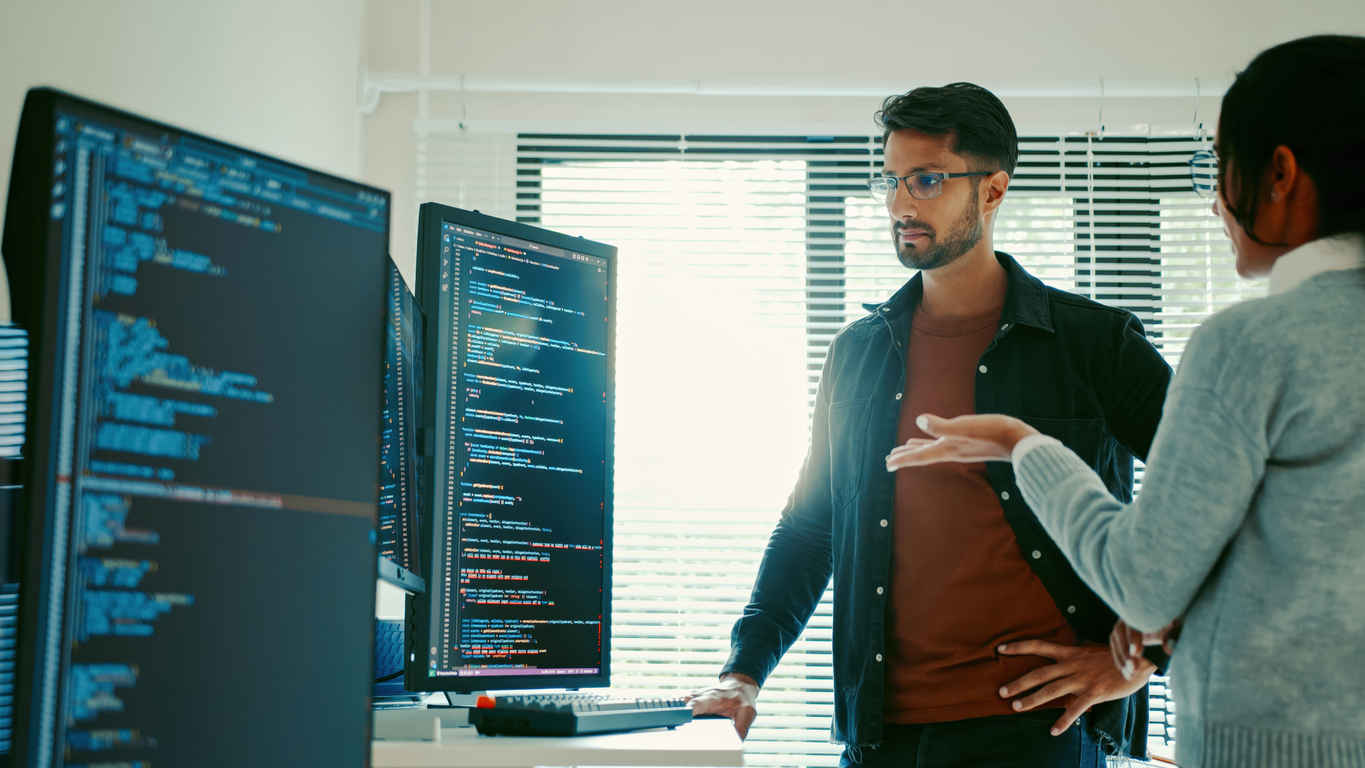 Two Security Operations Professionals Review Code on a Monitor.