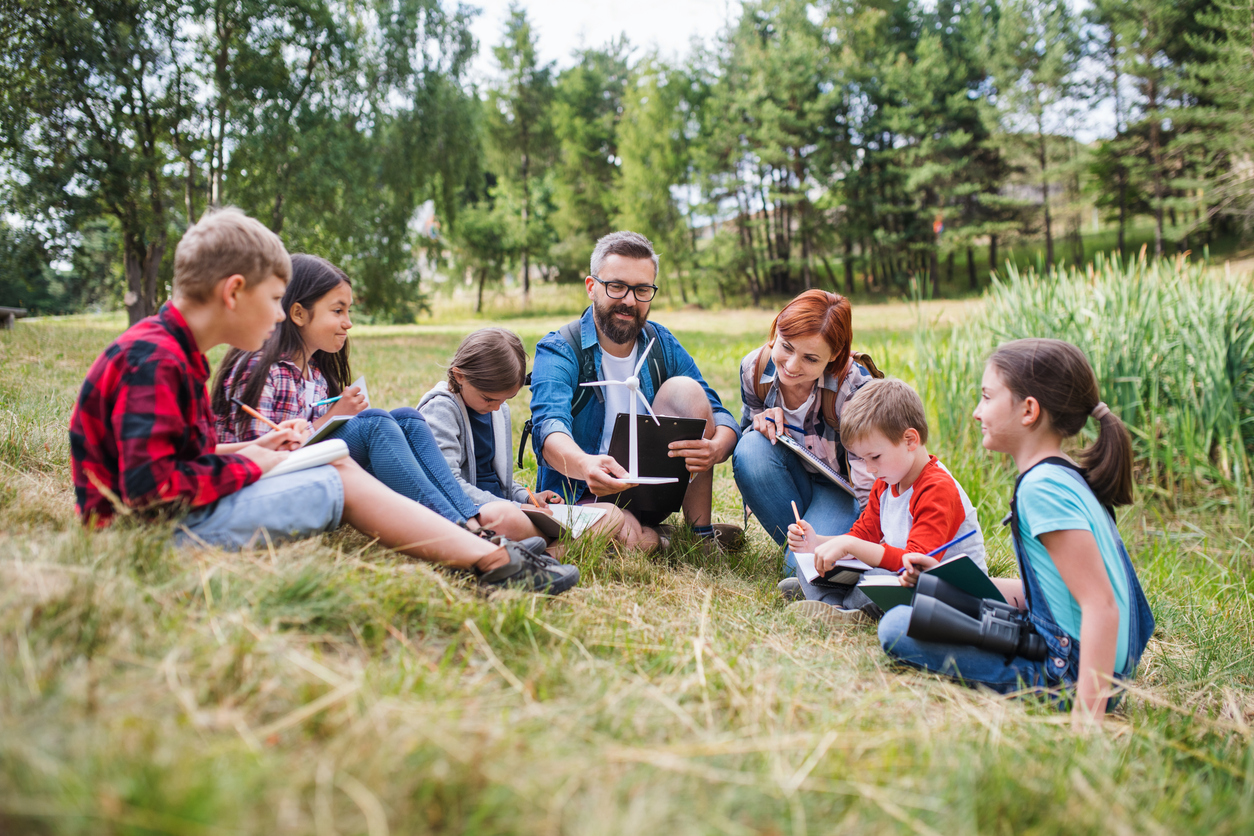 A Teacher Holding a Windmill Model Talking to a Group of Students Outside.